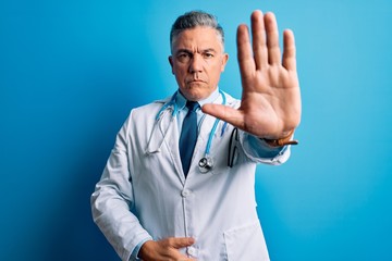 Middle age handsome grey-haired doctor man wearing coat and blue stethoscope doing stop sing with...
