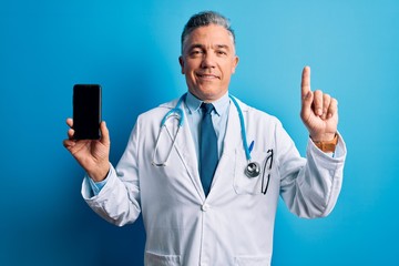 Middle age handsome grey-haired doctor man holding smartphone showing screen surprised with an idea or question pointing finger with happy face, number one