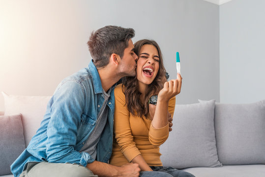 Happy couple looking at positive results of pregnancy test, planning future family life with child. Happy couple looking at pregnancy test on bed. Couple finding out results of a pregnancy test