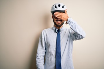 Young businessman wearing glasses and bike helmet standing over isolated white bakground smiling and laughing with hand on face covering eyes for surprise. Blind concept.