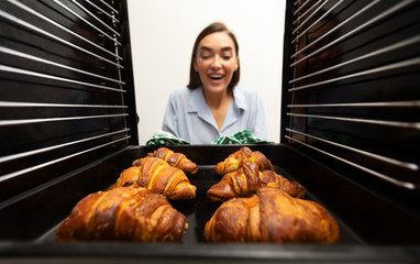 Cheerful woman taking delicious crispy croissants from oven