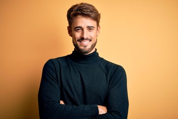 Young handsome man with beard wearing turtleneck sweater standing over yellow background happy face...