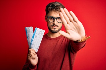 Young tourist man on vacation holding boarding pass standing over red bakground with open hand...