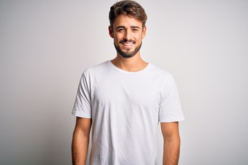 Young handsome man with beard wearing casual t-shirt standing over white background with a happy...
