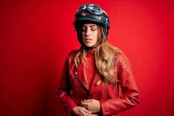 Young beautiful brunette motrocyclist woman wearing moto helmet over red background with hand on stomach because indigestion, painful illness feeling unwell. Ache concept.
