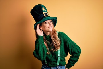 Beautiful brunette woman wearing green hat with clover celebrating saint patricks day smiling with hand over ear listening an hearing to rumor or gossip. Deafness concept.