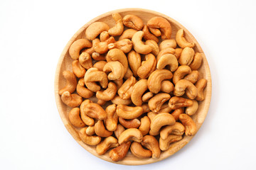 Cashew nuts on a wooden plate isolated on white background.