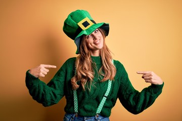 Beautiful brunette woman wearing green hat with clover celebrating saint patricks day looking confident with smile on face, pointing oneself with fingers proud and happy.