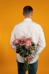 Back view of young man holding bouquet isolated on yellow background