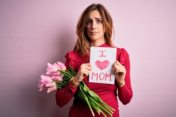 Beautiful brunette woman holding love mom message and tulips celebrating mothers day with a confident expression on smart face thinking serious