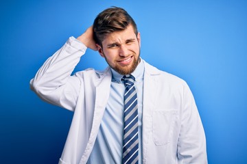 Young blond therapist man with beard and blue eyes wearing coat and tie over background confuse and wonder about question. Uncertain with doubt, thinking with hand on head. Pensive concept.