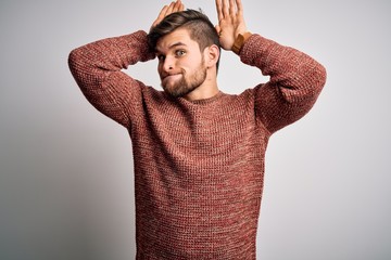 Young blond man with beard and blue eyes wearing casual sweater over white background Doing bunny ears gesture with hands palms looking cynical and skeptical. Easter rabbit concept.
