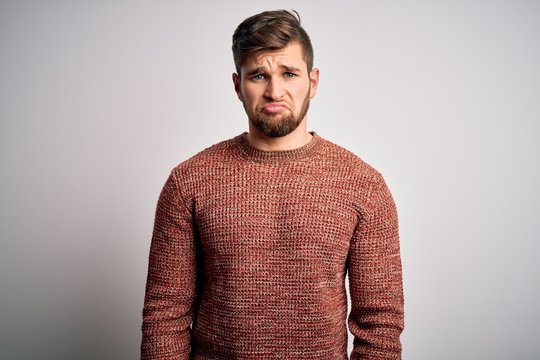 Young blond man with beard and blue eyes wearing casual sweater over white background depressed and worry for distress, crying angry and afraid. Sad expression.