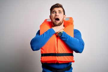 Young blond tourist man with beard and blue eyes wearing lifejacket over white background shouting...