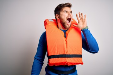 Young blond tourist man with beard and blue eyes wearing lifejacket over white background shouting...
