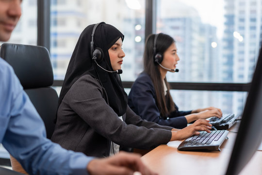 Arabian or Muslim woman works in a call center operator and customer service agent wearing microphone headsets working on computer in a call , talking with customer for assisting