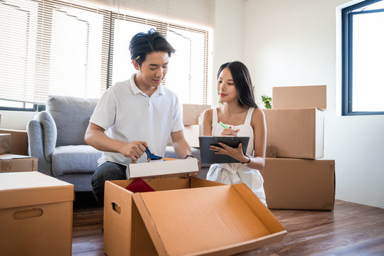 Young beautiful asian couple in love moving to new home, sitting on the floor very happy and cheerful for new apartment around cardboard boxes and holding cardboard boxes while moving home