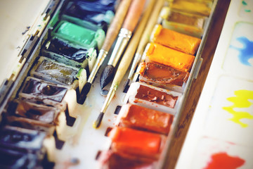 Four soft brushes of different sizes lie in a set with a multicolor bright artistic watercolor, illuminated by a bright light.