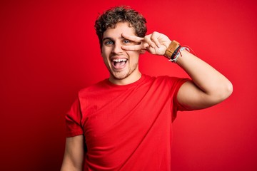 Fototapeta na wymiar Young blond handsome man with curly hair wearing casual t-shirt over red background Doing peace symbol with fingers over face, smiling cheerful showing victory