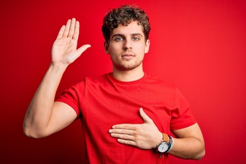 Young blond handsome man with curly hair wearing casual t-shirt over red background Swearing with...