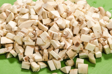 Sliced champignon mushrooms on a green board on a white background