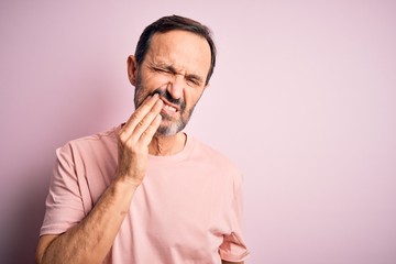 Middle age hoary man wearing casual t-shirt standing over isolated pink background touching mouth with hand with painful expression because of toothache or dental illness on teeth. Dentist