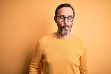 Middle age hoary man wearing casual sweater and glasses over isolated yellow background making fish face with lips, crazy and comical gesture. Funny expression.