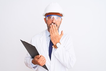 Senior engineer man wearing helmet glasses holding clipboard over isolated white background cover mouth with hand shocked with shame for mistake, expression of fear, scared in silence, secret concept