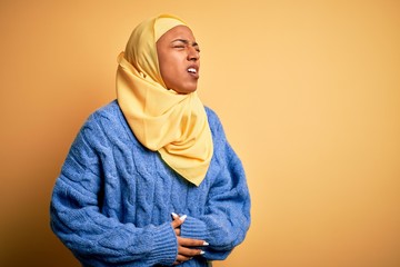 Young African American afro woman wearing muslim hijab over isolated yellow background with hand on...
