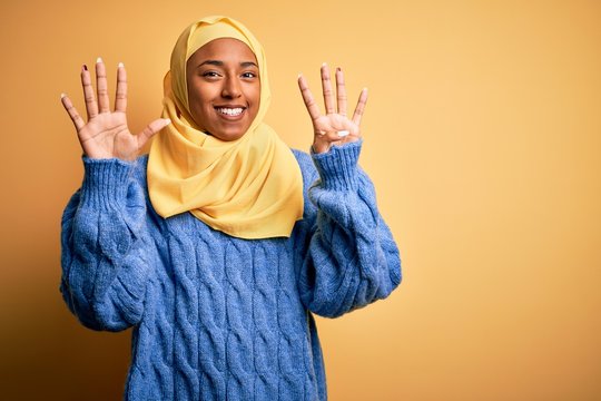 Young African American afro woman wearing muslim hijab over isolated yellow background showing and pointing up with fingers number nine while smiling confident and happy.