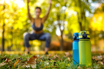 two bottles of water on green grass. sporty woman doing outdoor workout in park on background. focus on bottle