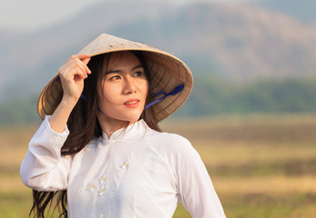 Portrait  vietnamese woman in a white dress wearing a Ao dai, walking happily in the evening meadow