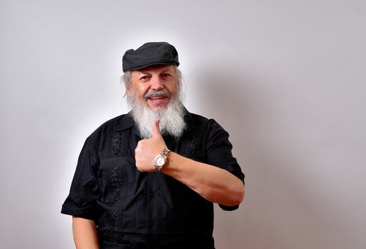 Happy old man is giving the thumbs up... .Mature gentleman with a newsboy cap and black guayabera shirt and long white beard..Happy old man with a big smile.
