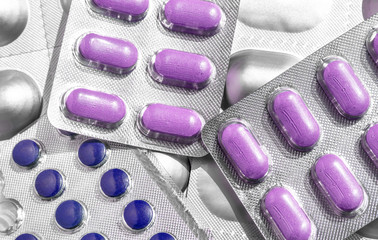 Lot of blisters with colored purple tablets of different shapes close-up