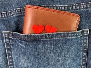 Men's wallet in the back pocket of jeans. Leather brown wallet in blue jeans. Two hearts on clothes.