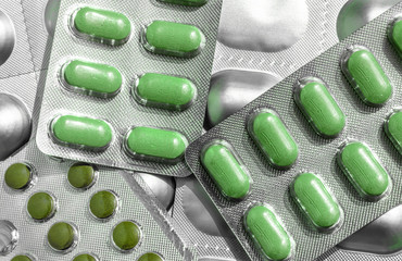 Several of blisters with colored green tablets of different shapes close-up