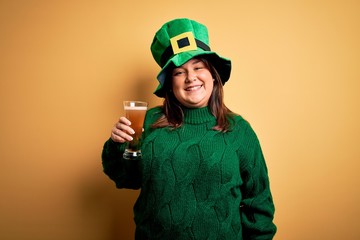 Young beautiful plus size woman wearing green hat celebrating st patricks day drinking beer with a happy face standing and smiling with a confident smile showing teeth
