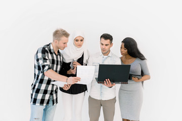Happy Casual Group Of Four Multiethnic People Standing Over White Background, using laptop and tablets while working together. Study, business, education concept