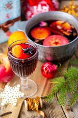 Mulled wine in a beautiful glass next to the saucepan. Hot drink in a glass. Christmas concept. Family evening with a hot drink. We cook mulled wine with apples and oranges. Hot wine.