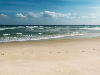Sandy seashore, calm soft waves at sea, sunny weather, blue sky with white clouds
