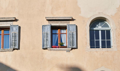 Italian windows on the yellow sandy color wall facade with wooden old and shabby grey colored shutters