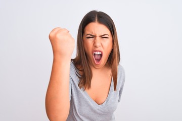 Portrait of beautiful young woman standing over isolated white background angry and mad raising fist frustrated and furious while shouting with anger. Rage and aggressive concept.
