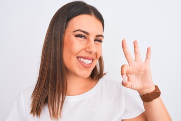 Close up of beautiful and young brunette woman standing over isolated white background doing ok sign with fingers, excellent symbol