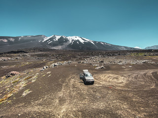 View on the Volcano Antuco in Chile (South America) surrounded by desert with 4x4 jeep parked in the foreground with tire tracks in the sand and snow on the top of the mountain