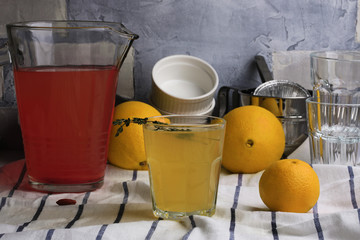 Red fruit drink in a jug. Glass cup with a yellow drink. Oranges. Kitchen background. Close-up.