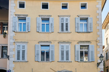 Eight italian windows on the yellow wall facade with wooden shabby white color shutters