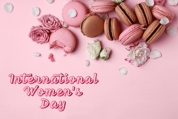 Different tasty macarons with flowers and text INTERNATIONAL WOMEN'S DAY on color background