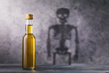 A bottle of whiskey with a shadow in the shape of a skeleton. Concept on the harm of alcohol and...