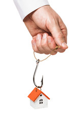 A man holds in his hand a fishing hook, for which a toy house is suspended. Concept on the topic of payment of mortgage lending. Isolated on a white background