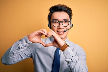 Young handsome chinese call center agent man wering glasses using headset smiling in love showing...